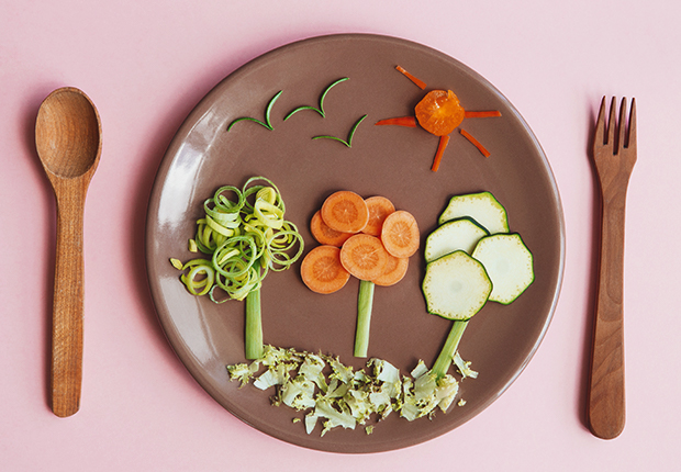 Plate, wooden spoon and fork, veggies on the plate arranged as trees and sky